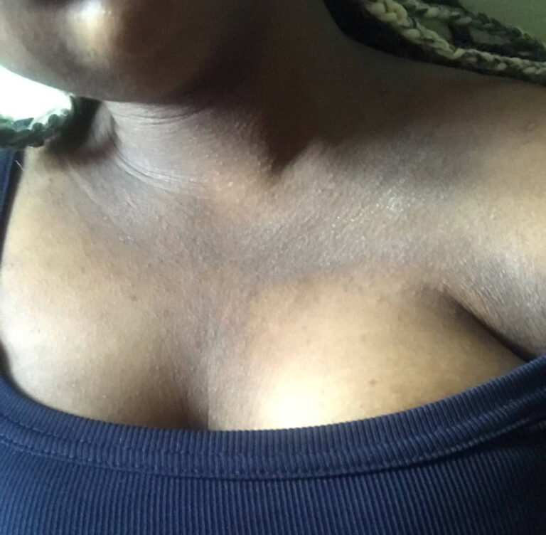 A close-up image of a person wearing a navy blue top, with the neckline slightly off the shoulder, revealing part of their chest and collarbone. The person's skin is medium to dark brown.